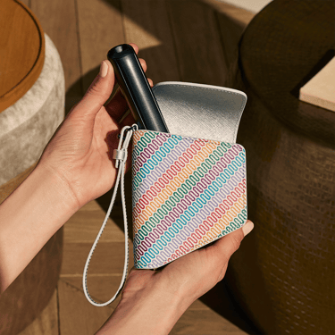 Ruka uzima Ploom AURA Jet Black uređaj i vadi iz Ploom Multicolored Patterned Canvas duo torbice