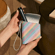 Ruka uzima Ploom AURA Jet Black uređaj i vadi iz Ploom Multicolored Patterned Canvas duo torbice 
